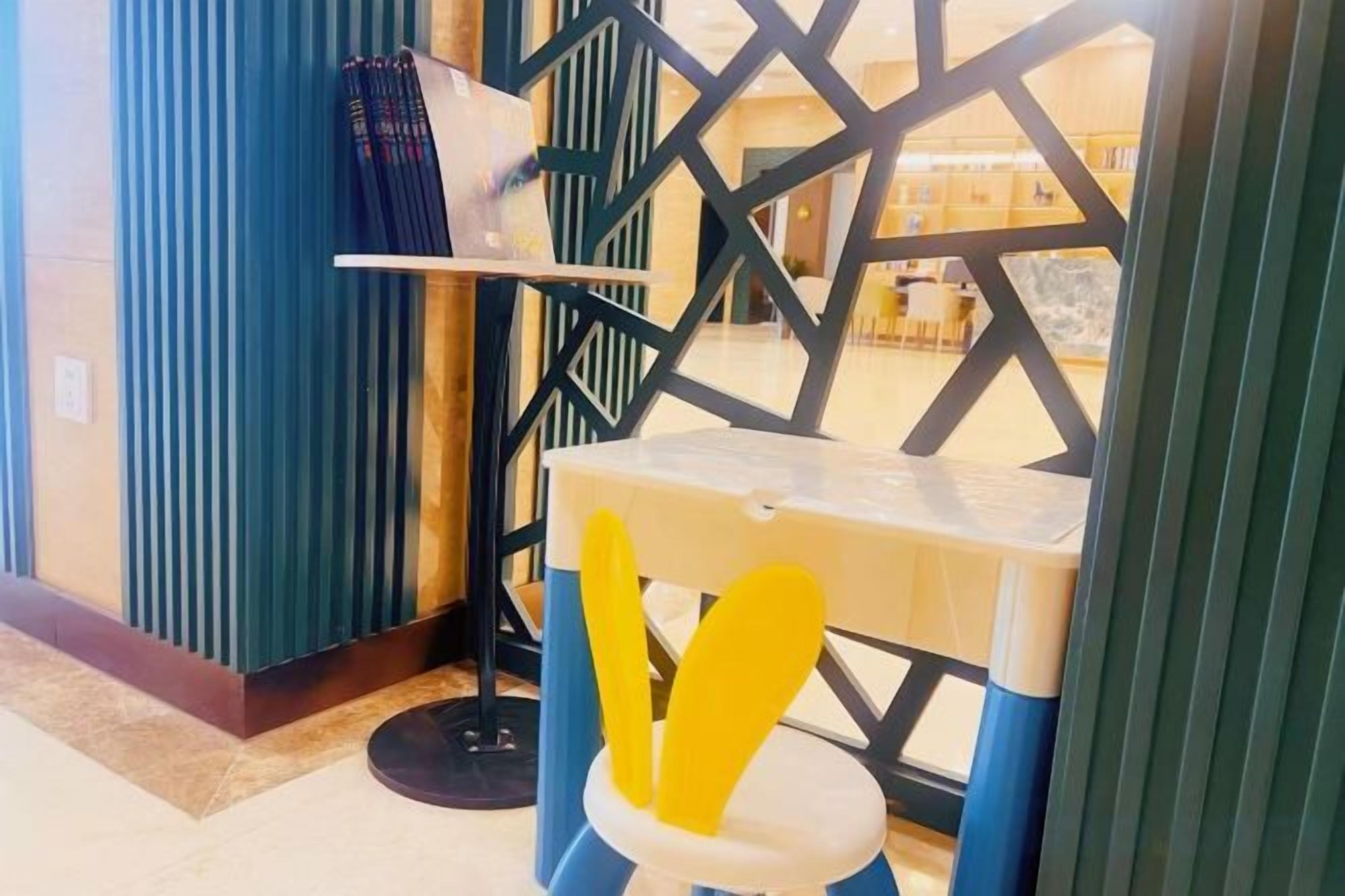 A corner of a room with a blue wall, a white table with yellow utensils, and a black floor lamp.