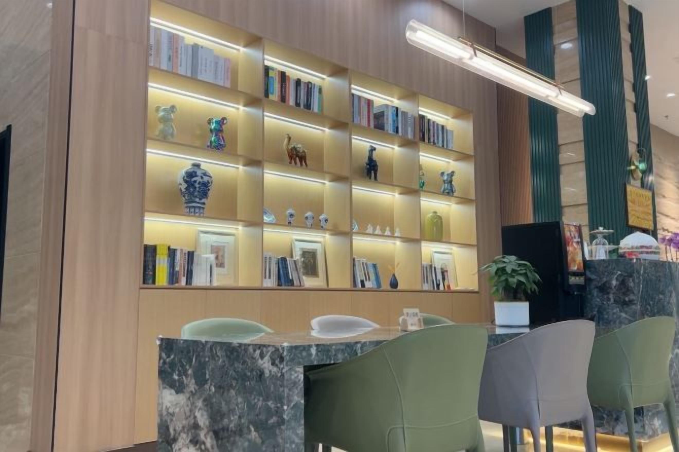 A reception area with a marble counter, green chairs, and a bookshelf with decorative items.