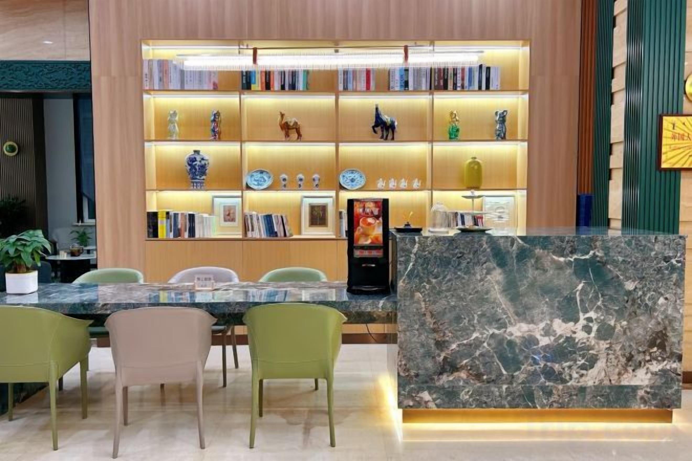 A reception area with a marble counter, green chairs, a bookshelf with decorative items, and a potted plant.