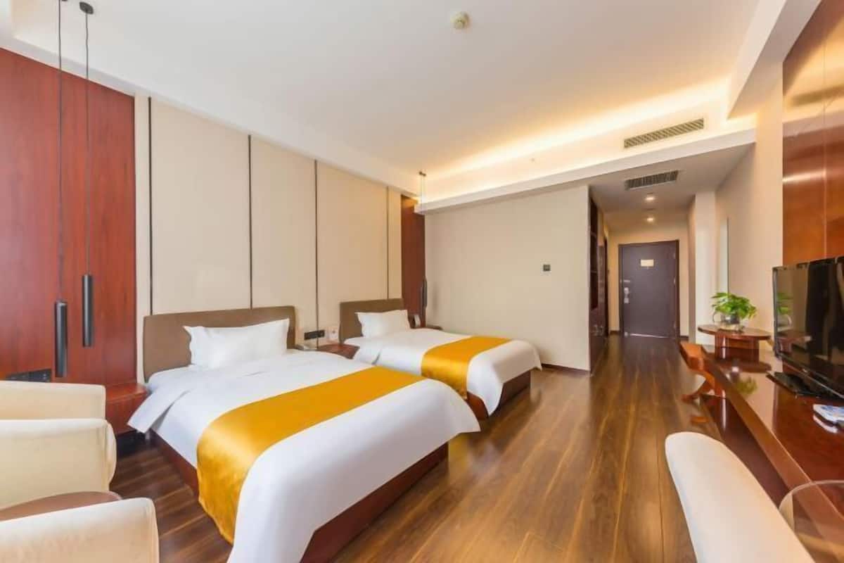 A hotel room with two beds, a wooden floor, a TV, and a desk with a chair.