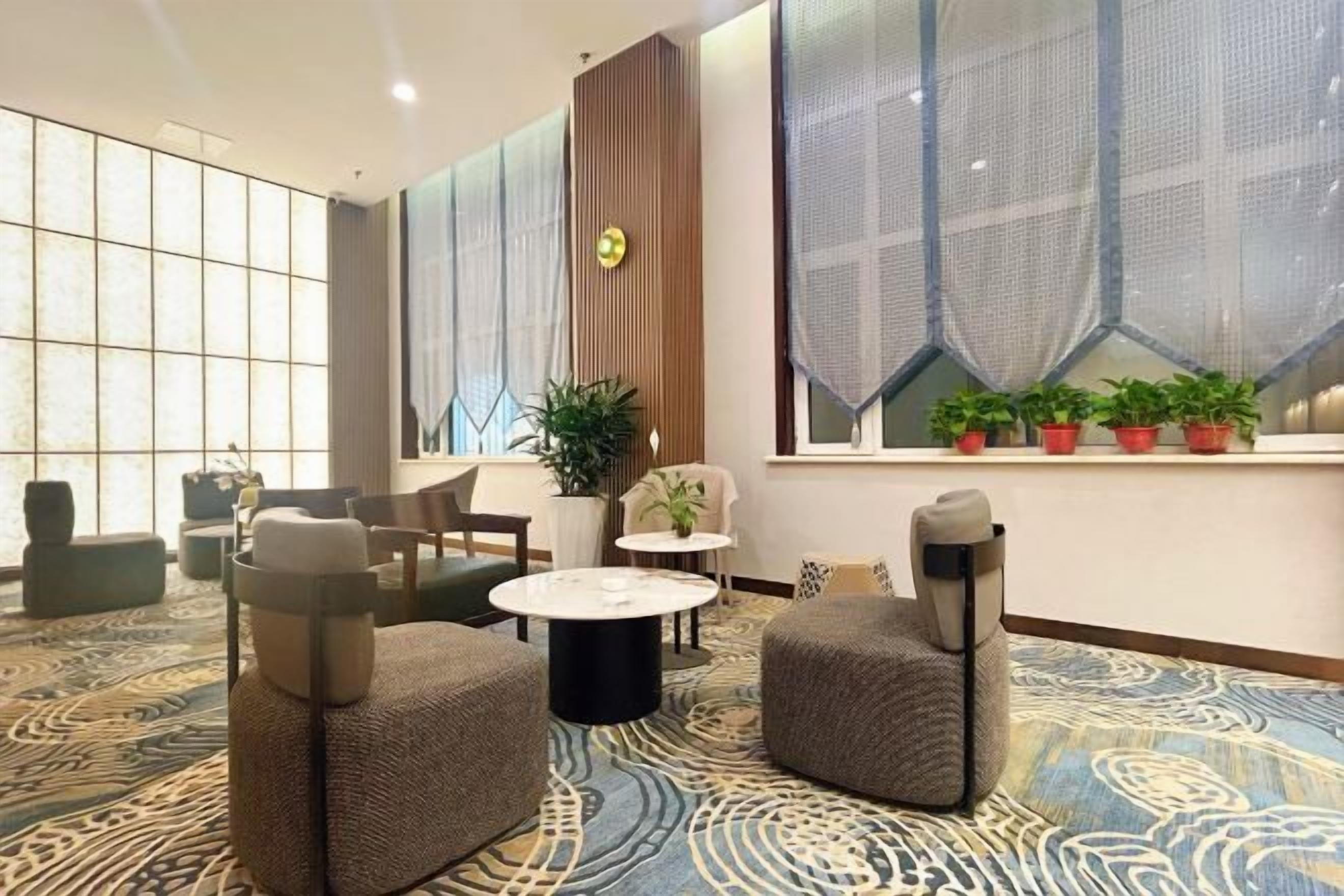 Eine Hotelhalle mit Sitzgelegenheiten, einem großen Fenster mit Pflanzen und einem gemusterten Teppich.