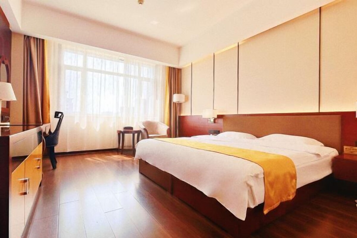 Une chambre d’hôtel avec un grand lit, un bureau, une chaise et une fenêtre avec des rideaux.