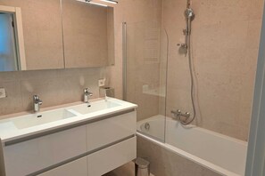 Ein modernes Badezimmer mit zwei Waschbecken, einer Duschkabine aus Glas und einer Badewanne.