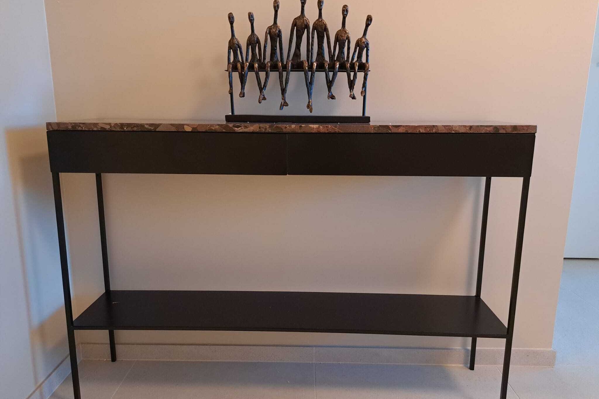 Una mesa de metal negro con un estante y una escultura decorativa encima.
