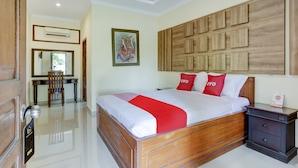 A hotel room with a wooden bed, a desk with a chair, a wall-mounted air conditioner, and a framed picture. - Hotel O D'lima Guest House Sub (Surabaya)
