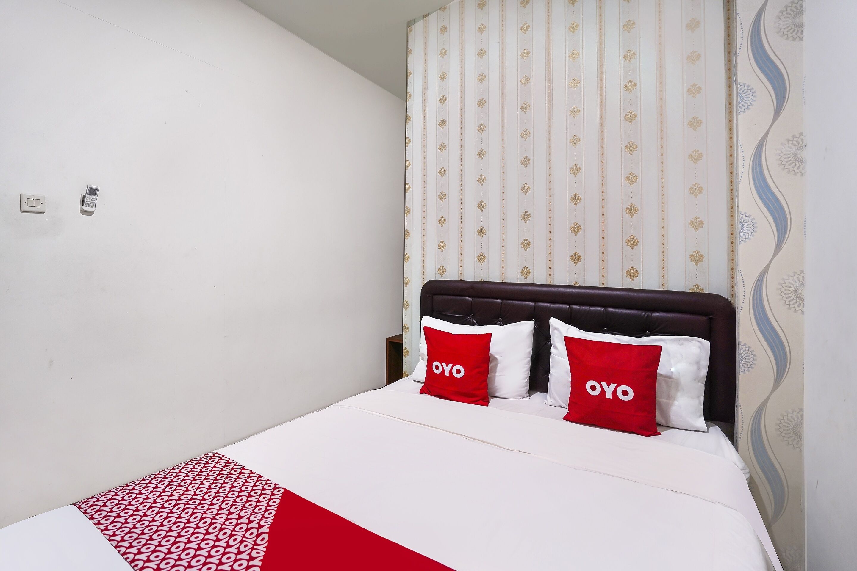 A neatly made bed with two red pillows, a white bedspread, and a patterned blanket.