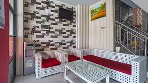 A room with a patterned wall, a flat-screen TV, a refrigerator, a sofa with red cushions, and a staircase. - Hotel O D'lima Guest House Sub (Surabaya)