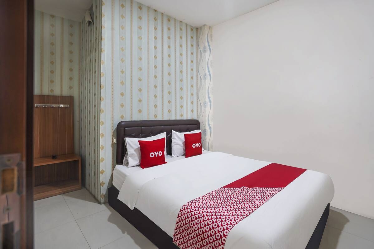A neatly made bed with a white and red bedspread, two pillows with the word "OYO" on them, and a wooden headboard.