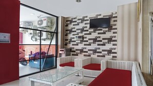 A room with a glass partition, white wicker furniture, a flat-screen TV, and patterned wall tiles. - Hotel O D'lima Guest House Sub (Surabaya)