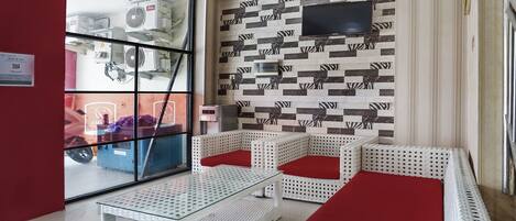A room with a glass partition, white wicker furniture, a flat-screen TV, and patterned wall tiles.