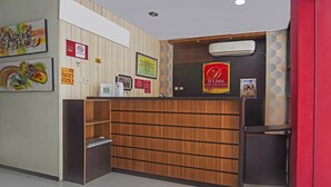 A reception area with a wooden reception desk, framed artwork on the walls, and a red sign indicating a D'Lim exclusive cost service. - Hotel O D'lima Guest House Sub (Surabaya)