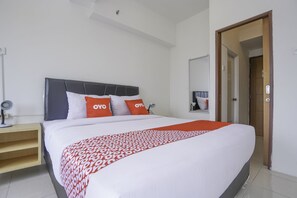 Een netjes opgemaakt bed met een bedsprei met patroon, een nachtkastje met een lamp, en een deur die naar een andere kamer leidt.