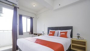A hotel room with a large bed, two bedside tables, a nightstand, a window with curtains, and a ceiling fan.