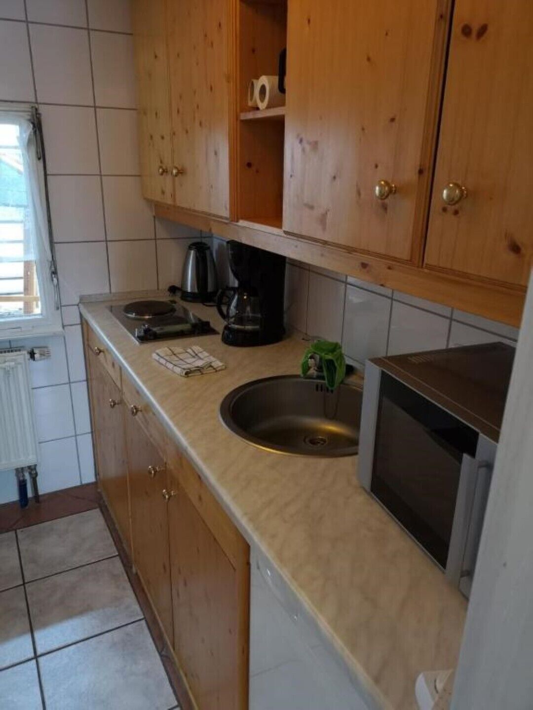 Een compacte keuken met houten kastjes, een roestvrijstalen spoelbak, een koffiezetapparaat en een vaatwasser.