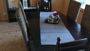A dining area with a dark wooden table and wicker chairs, a small white cabinet with decorative items, and a window with natural light. - Amy's vacation home (Simmerath)