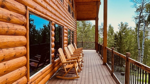A wooden log cabin with a porch featuring rocking chairs and a view of the surrounding forest.