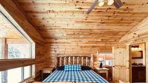 A log cabin bedroom with a wooden bed, a window, and a wooden ceiling.