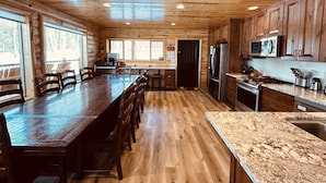 A spacious kitchen with wooden cabinets, a long dining table, and a granite countertop.