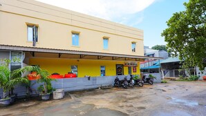 A building with a yellow facade, a covered parking area, and several potted plants. - OYO 91659 City Residence (Batam)