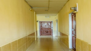 A corridor with yellow walls and tiled floors, leading to a door with a metal frame and a small sign above it. - OYO 91659 City Residence (Batam)