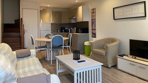 A compact living space with a kitchenette, a dining area, a sofa, a TV, and a staircase. - Charming fisherman's cottage (Saint-Valery-en-Caux)