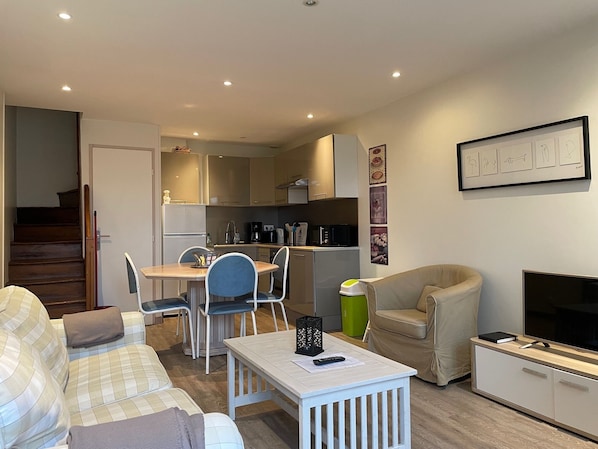 A compact living space with a kitchenette, a dining area, a sofa, a TV, and a staircase.