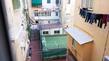 A narrow urban street with buildings on either side, a visible tennis court, and clothes hanging on a line.