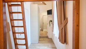A wooden ladder leading to a bathroom with a shower, a towel hanging on the wall, and a television mounted above the shower. - Toto e Peppino luxury rooms (Naples)