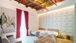 A modern hotel room with a wooden ceiling, a large bed, a sofa, a dining table, and a wall-mounted air conditioner. - Toto e Peppino luxury rooms (Naples)