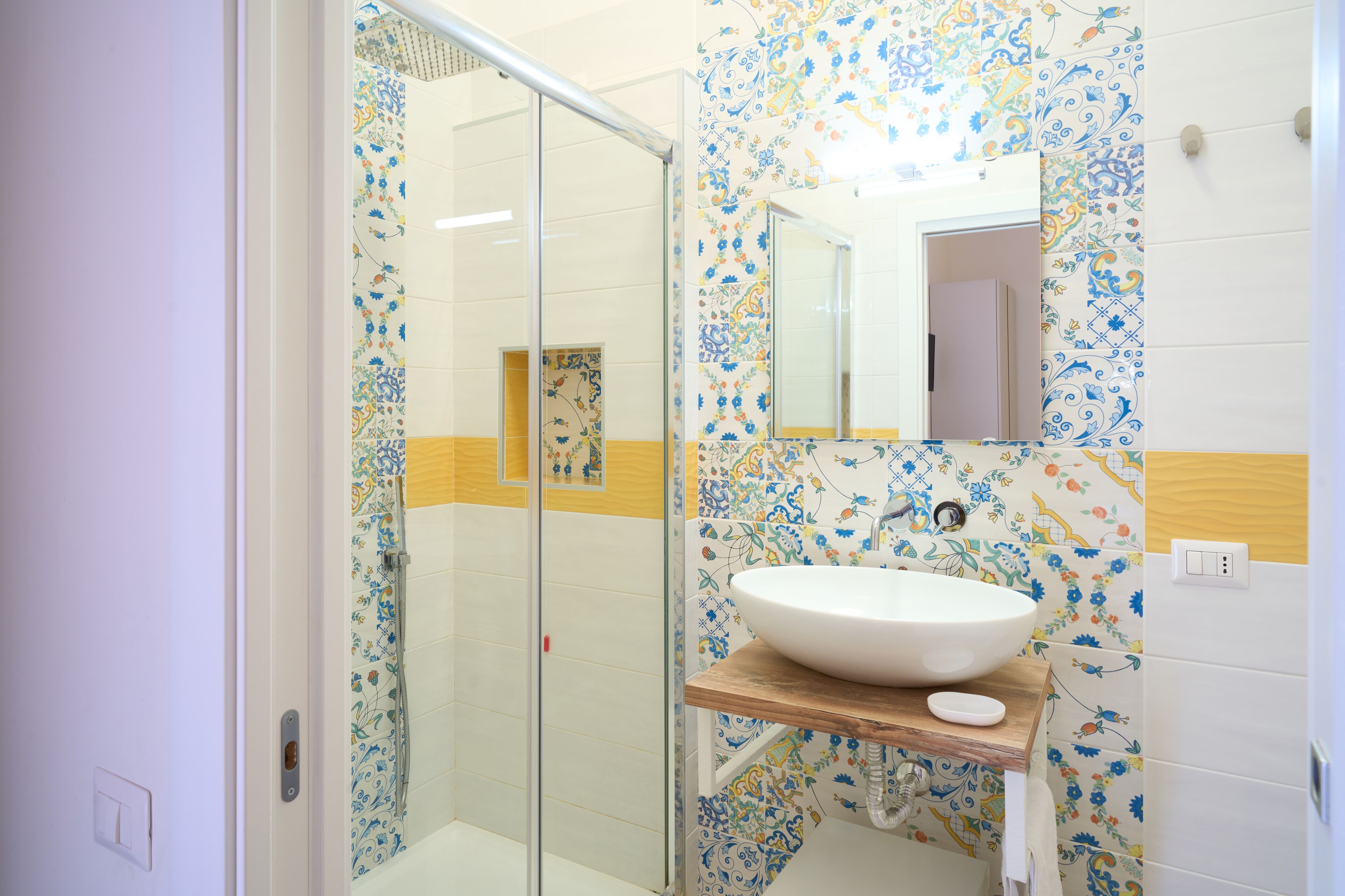 A bathroom with a glass shower enclosure, a white sink with a wooden countertop, and patterned tiles.