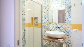 A bathroom with a glass shower enclosure, a white sink with a wooden countertop, and patterned tiles.