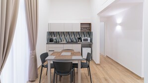 A compact kitchen with a microwave, sink, and cabinets. There is a dining table with chairs and a patterned backsplash. - Toto e Peppino luxury rooms (Naples)