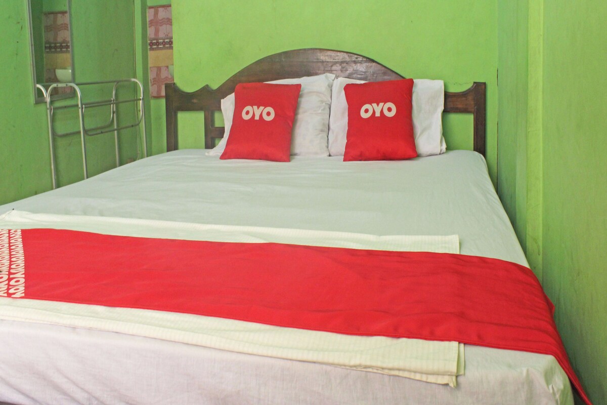 A bed with a wooden headboard, two red pillows with the word 'OYO' on them, and a red and white blanket.