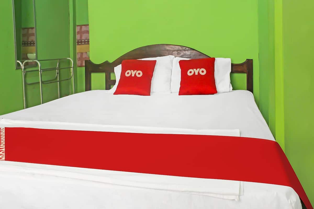 Un lit avec une couvre-lit rouge et blanche, deux oreillers portant le logo « OYO », et une tête de lit en bois.