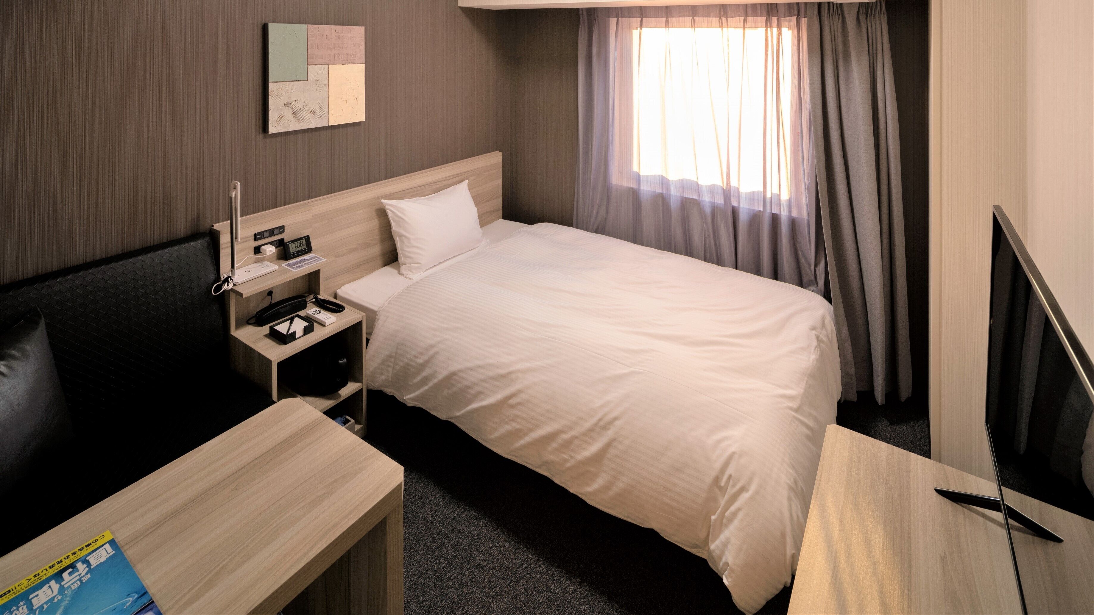 Hotellihuone, jossa on sänky, yöpöytä, televisio ja pieni työpöytä tuolilla.