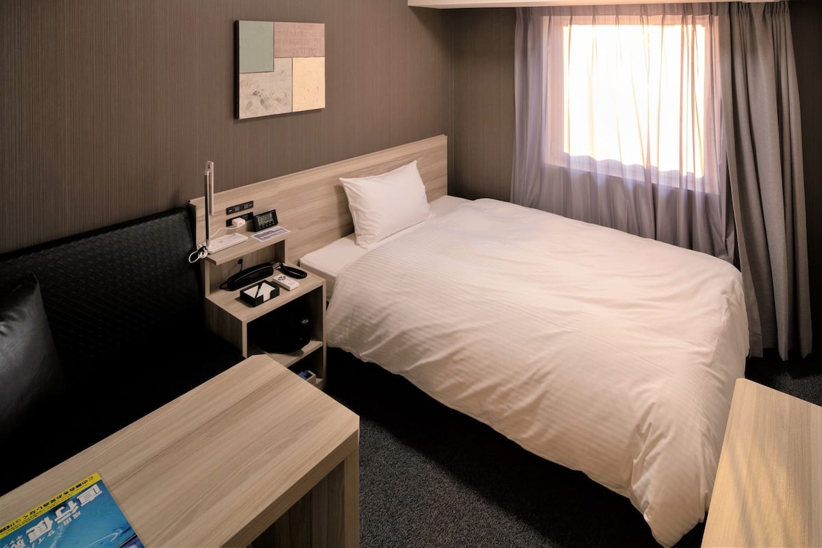 A hotel room with a bed, bedside table, TV, and a small desk with a chair.