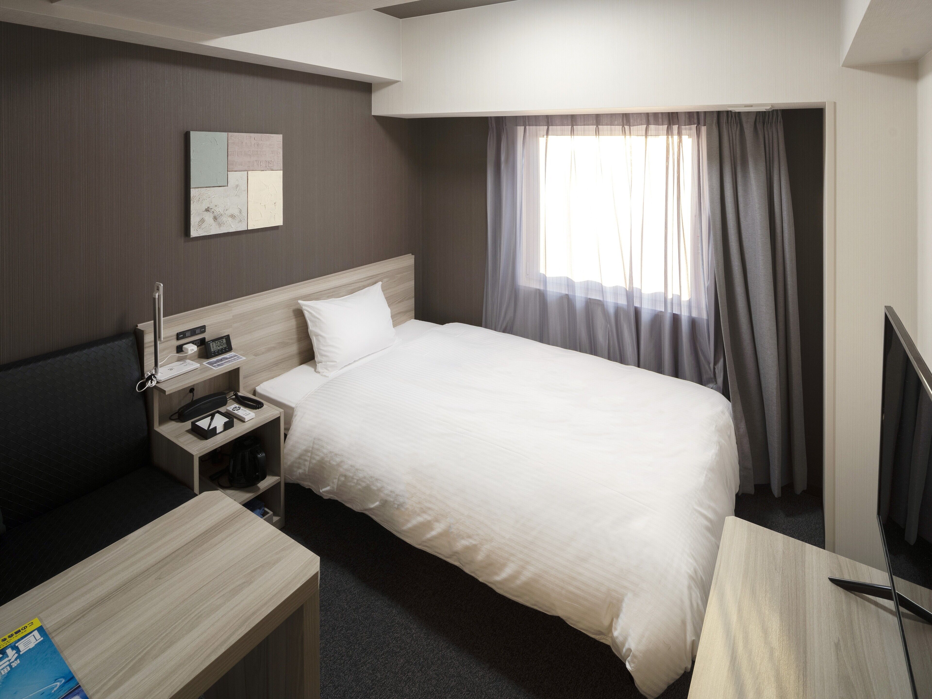 A hotel room with a bed, bedside table, lamp, and a window with curtains.