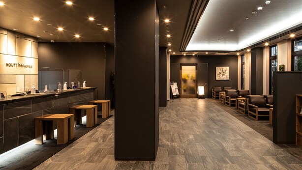 A modern hotel lobby with a reception desk, seating area, and a large pillar. - Hotel Route Inn Matsuyama Chuo -Katsuyama Dori- (Matsuyama)