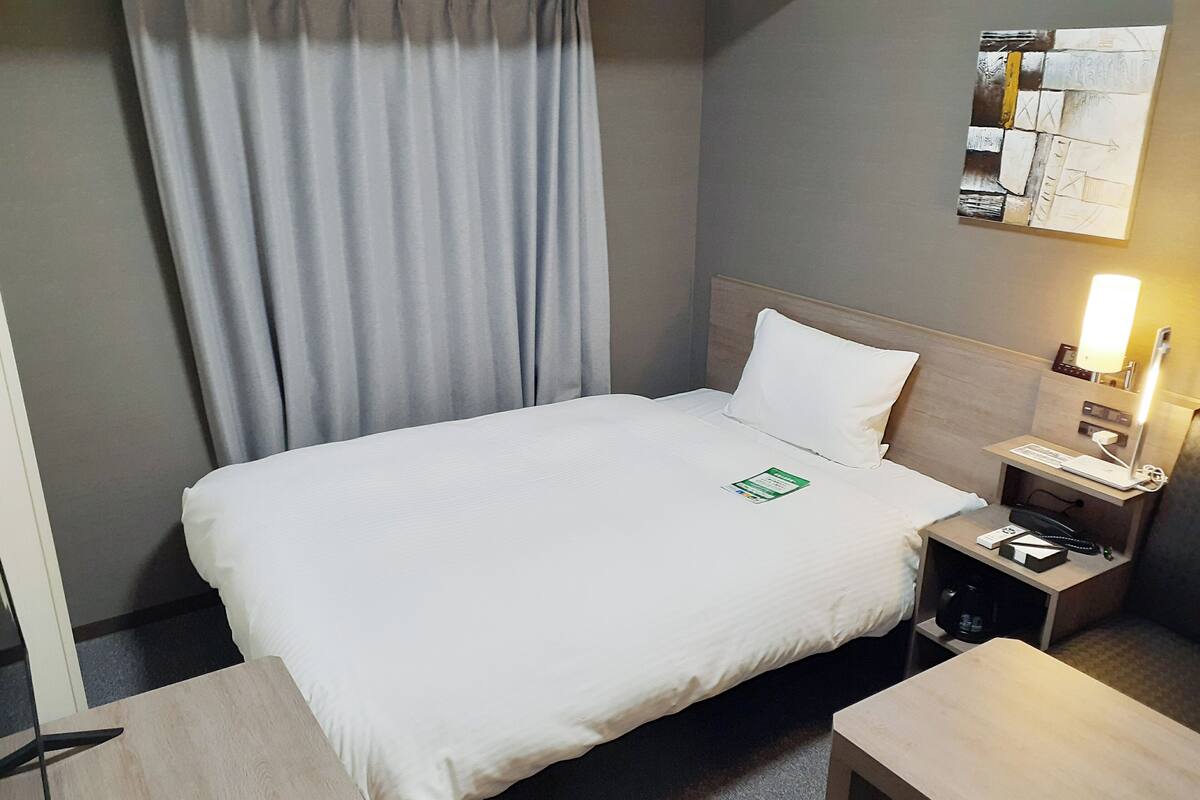Ein Hotelzimmer mit einem Bett, einem Nachttisch, einer Lampe und einem an der Wand montierten Bedienfeld.
