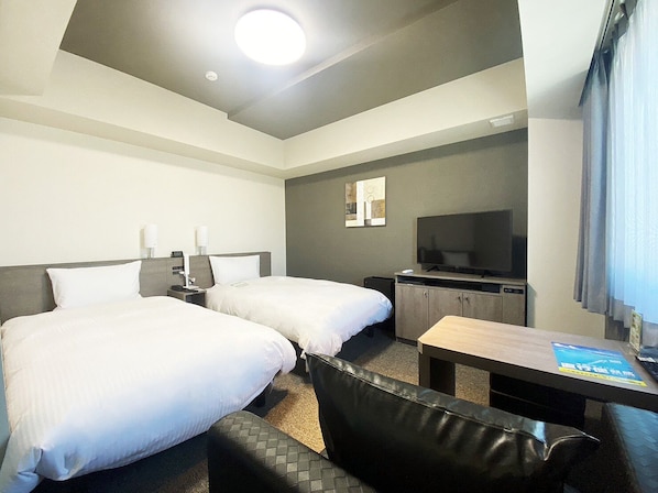 Ett hotellrum med två sängar, ett skrivbord, en tv och ett fönster med gardiner.