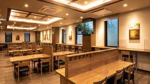 A modern dining area with wooden tables and chairs, a large TV screen, and artwork on the walls. - Hotel Route Inn Matsuyama Chuo -Katsuyama Dori- (Matsuyama)