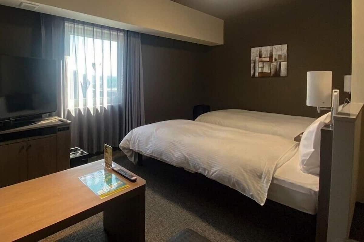 Ein Hotelzimmer mit Bett, Schreibtisch, Fernseher und einem fenster mit Vorhängen.