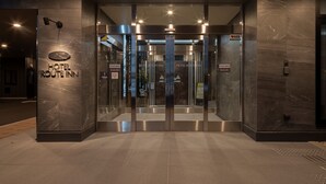 The entrance to Hotel Route Inn with a modern design, featuring a glass door entrance, a digital elevator display, and a sign indicating 'Cool Biz' and 'Warm Biz' temperature settings. - Hotel Route Inn Matsuyama Chuo -Katsuyama Dori- (Matsuyama)