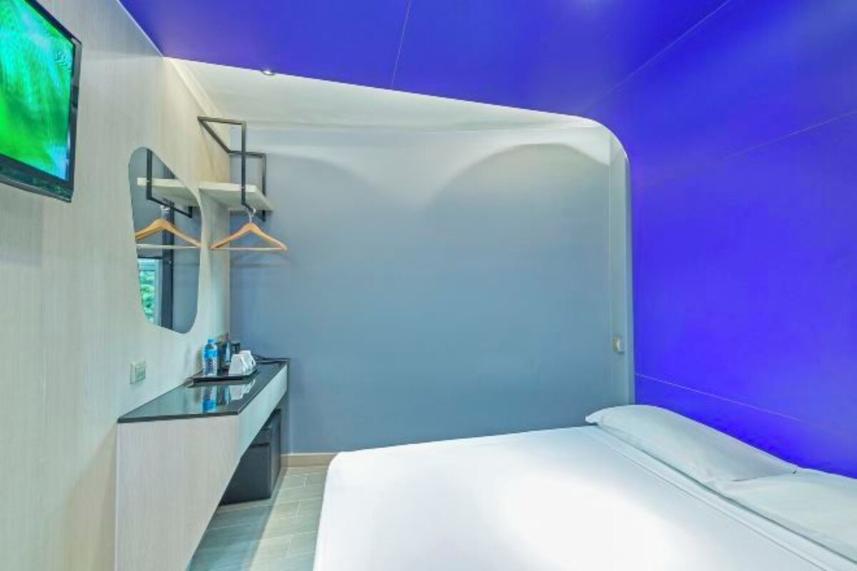 Habitación de hotel moderna con una cama curvada, un televisor de pantalla plana, un tocador con espejo y lavamanos, y una pared de acento azul.