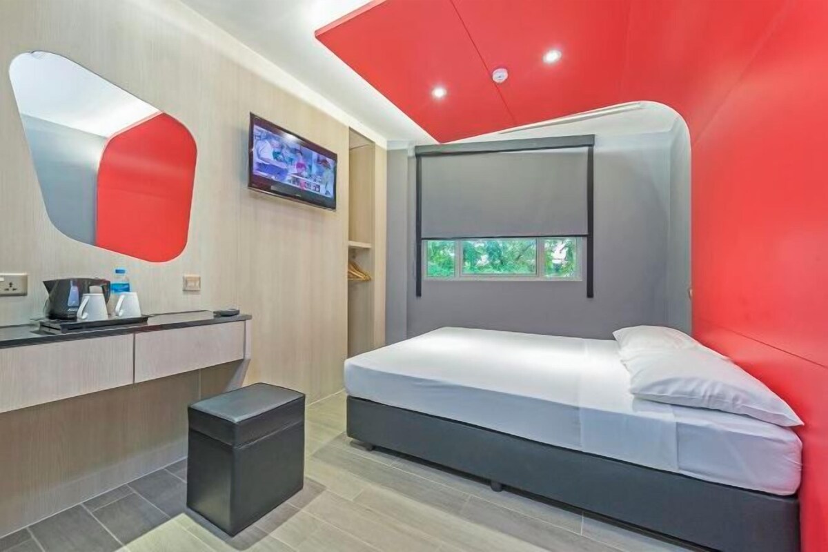 A modern bedroom with a bed, a TV mounted on the wall, and a window with a view of greenery.