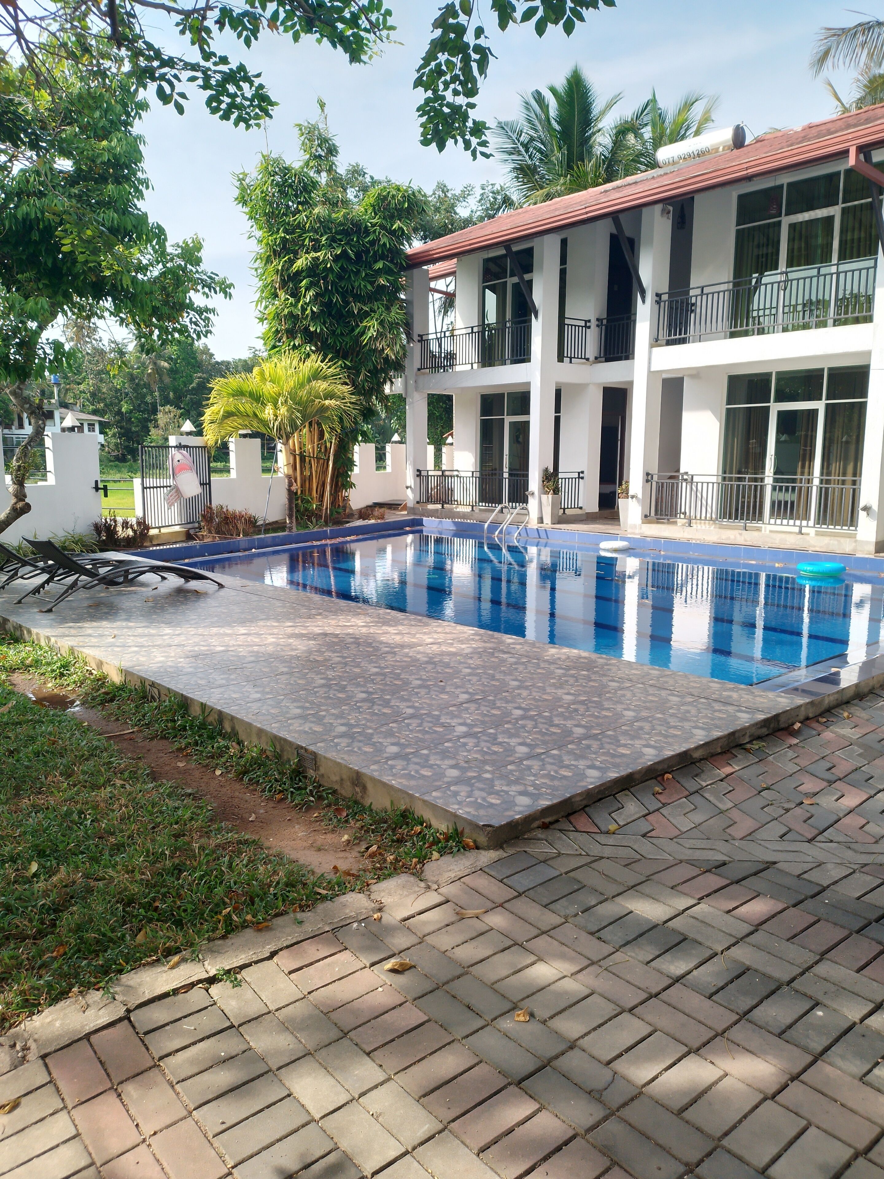 Una piscina con borde de baldosas, rodeada de follaje y un edificio de dos pisos con balcones.