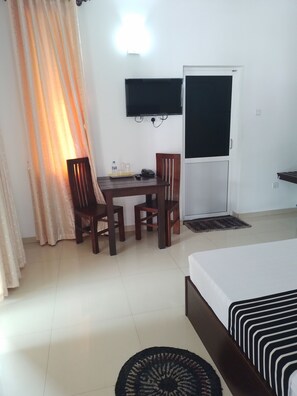 A hotel room with a bed, a desk with chairs, a television mounted on the wall, and a door. - Sanri villa Katunayaka (Seeduwa - Katunayake)