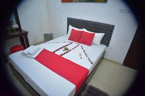 A neatly made bed with a white and red bedspread, a headboard, and a small table with a red stool beside it. - Sanri villa Katunayaka (Seeduwa - Katunayake)
