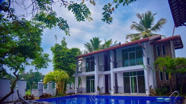 Un edificio de varios pisos con piscina, rodeado de vegetación y palmeras.