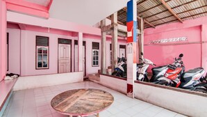 A pink-walled room with a tiled floor, a round wooden table, and several parked scooters. - Hotel O Raja Homestay Syariah (Pekanbaru)